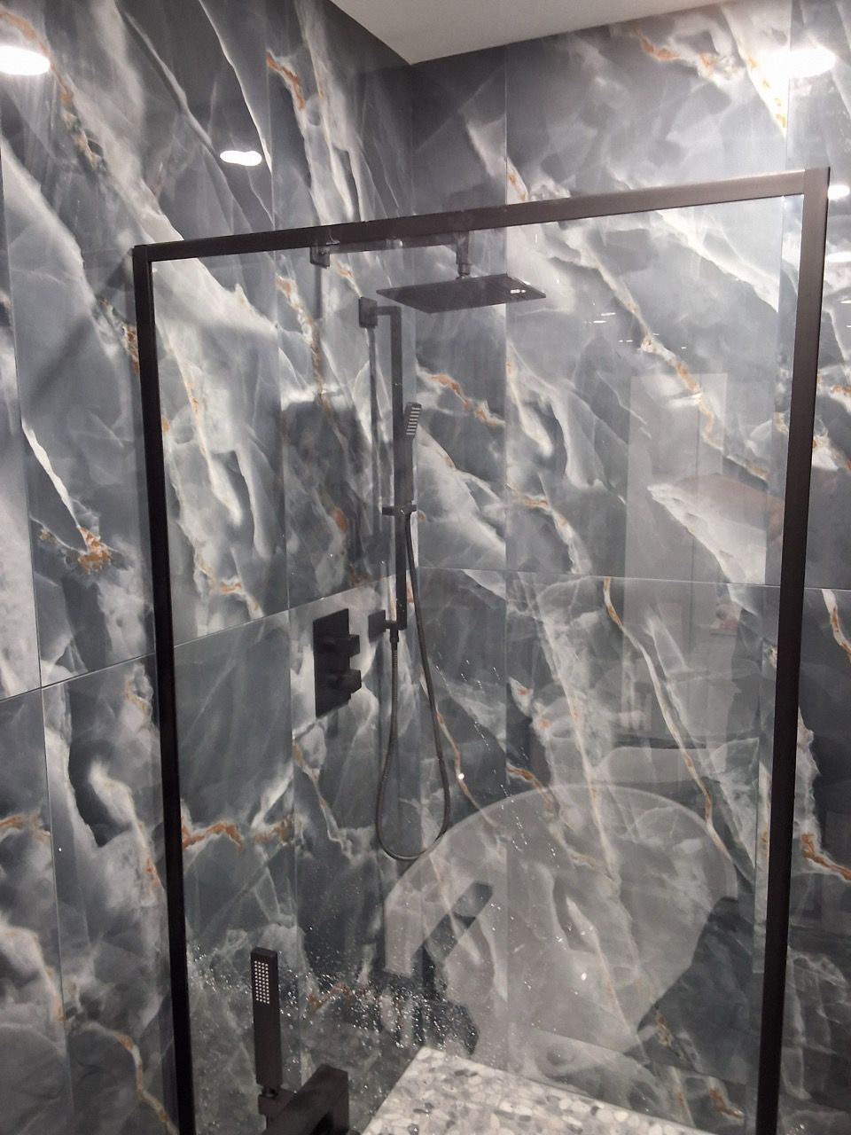 Glass shower enclosure with a metal frame against gray marble-like tiled walls.