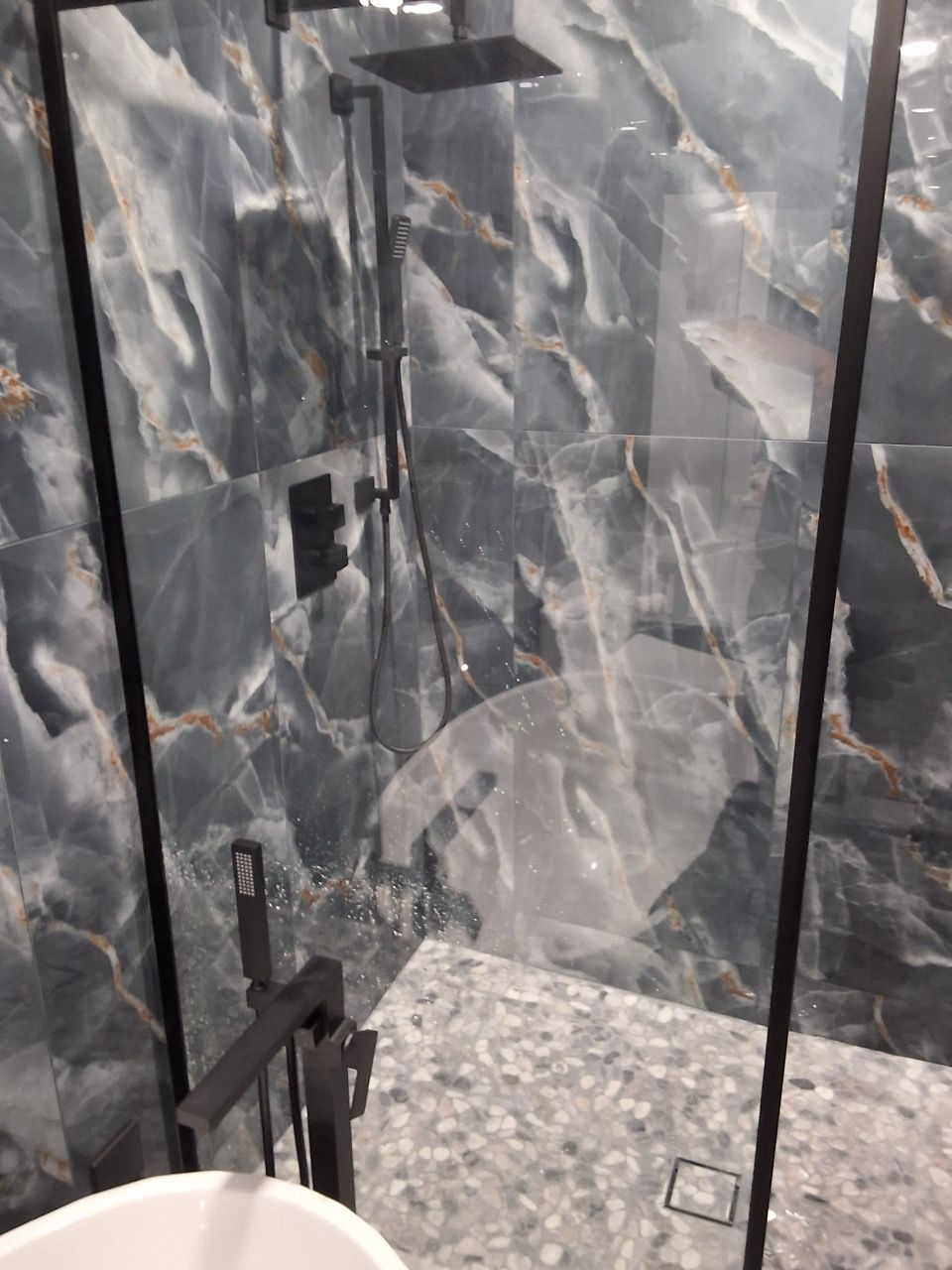 Marble-tiled bathroom shower with glass door and a built-in shelf.