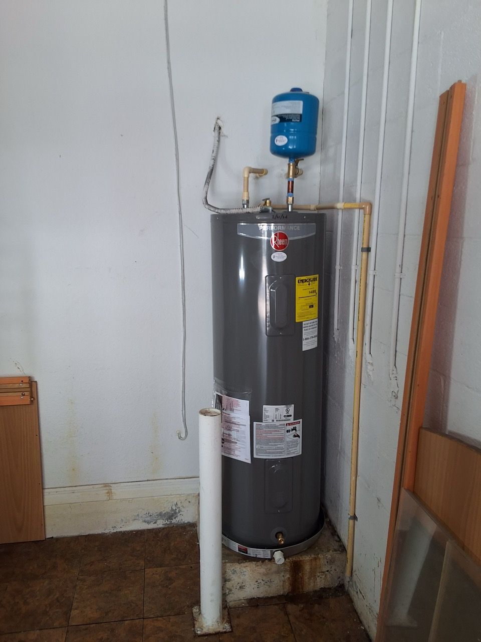 Residential water heater with blue expansion tank and exposed pipes in a utility corner