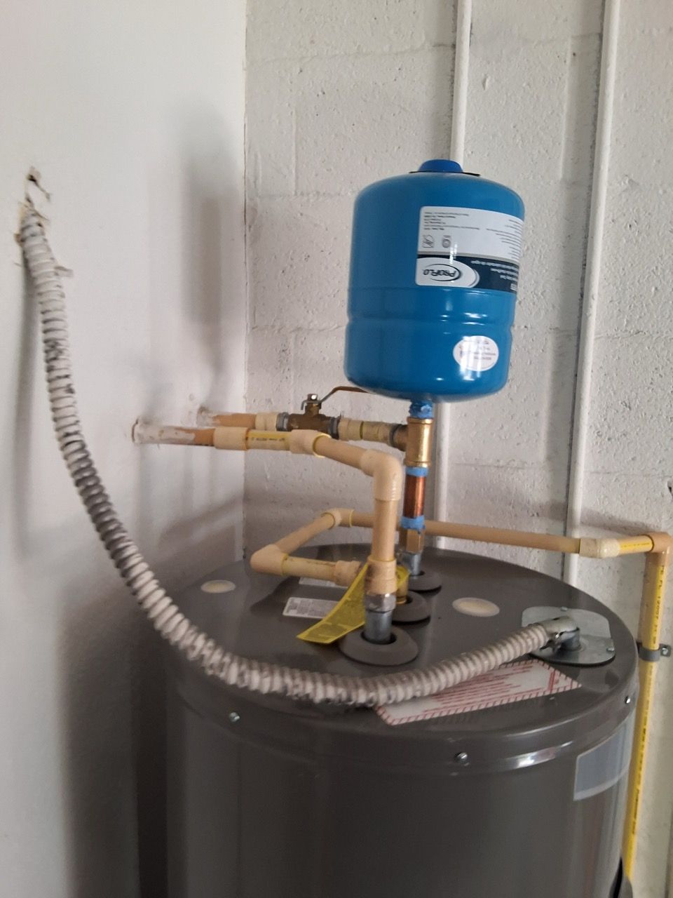 Water heater with pipes and a blue expansion tank against a wall