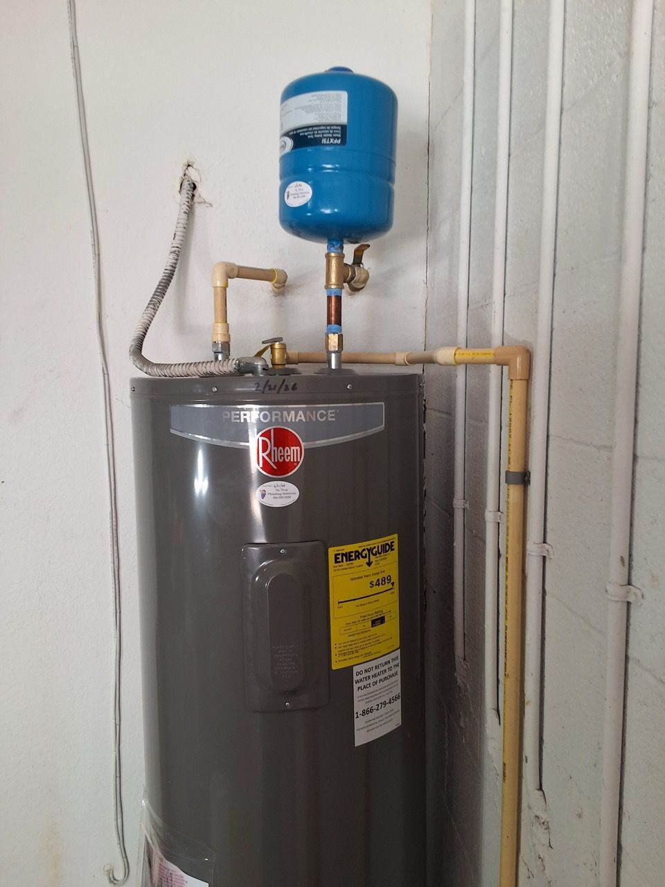 Gray water heater with blue expansion tank and copper pipes against a corrugated wall