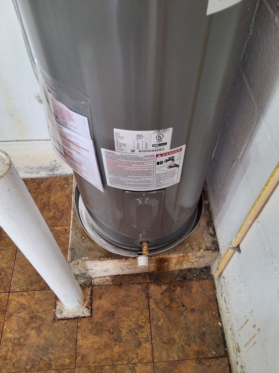 Water heater with labels and a drain valve in a small utility closet.