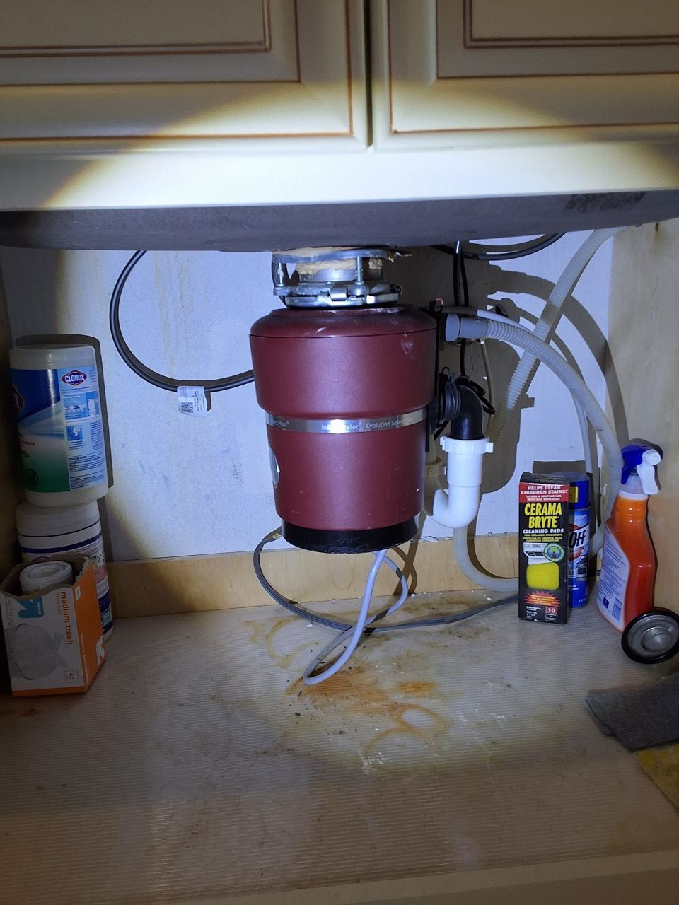 Under-sink water filter with red canister, tubing, and cleaning supplies in a cabinet