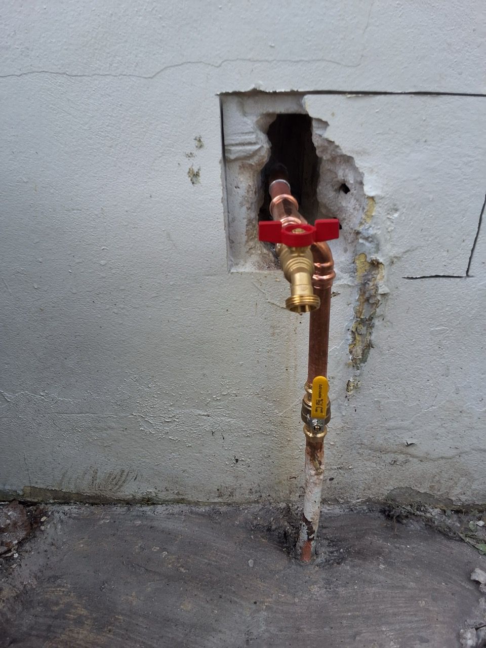 Red valve on exposed pipe protruding through a hole in a gray wall.