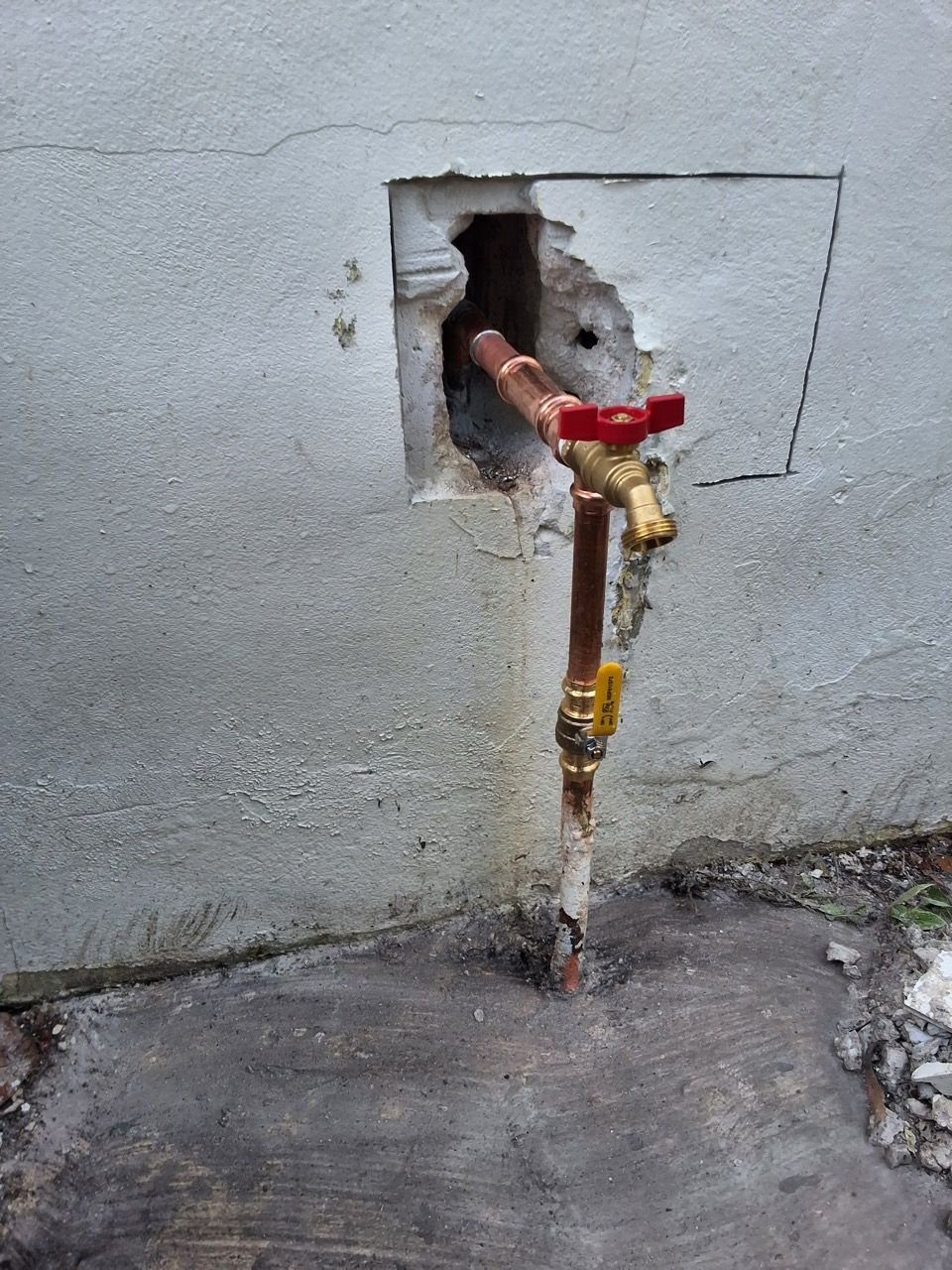 Exposed wall pipe with red-handled valve and water meter on a gray concrete wall