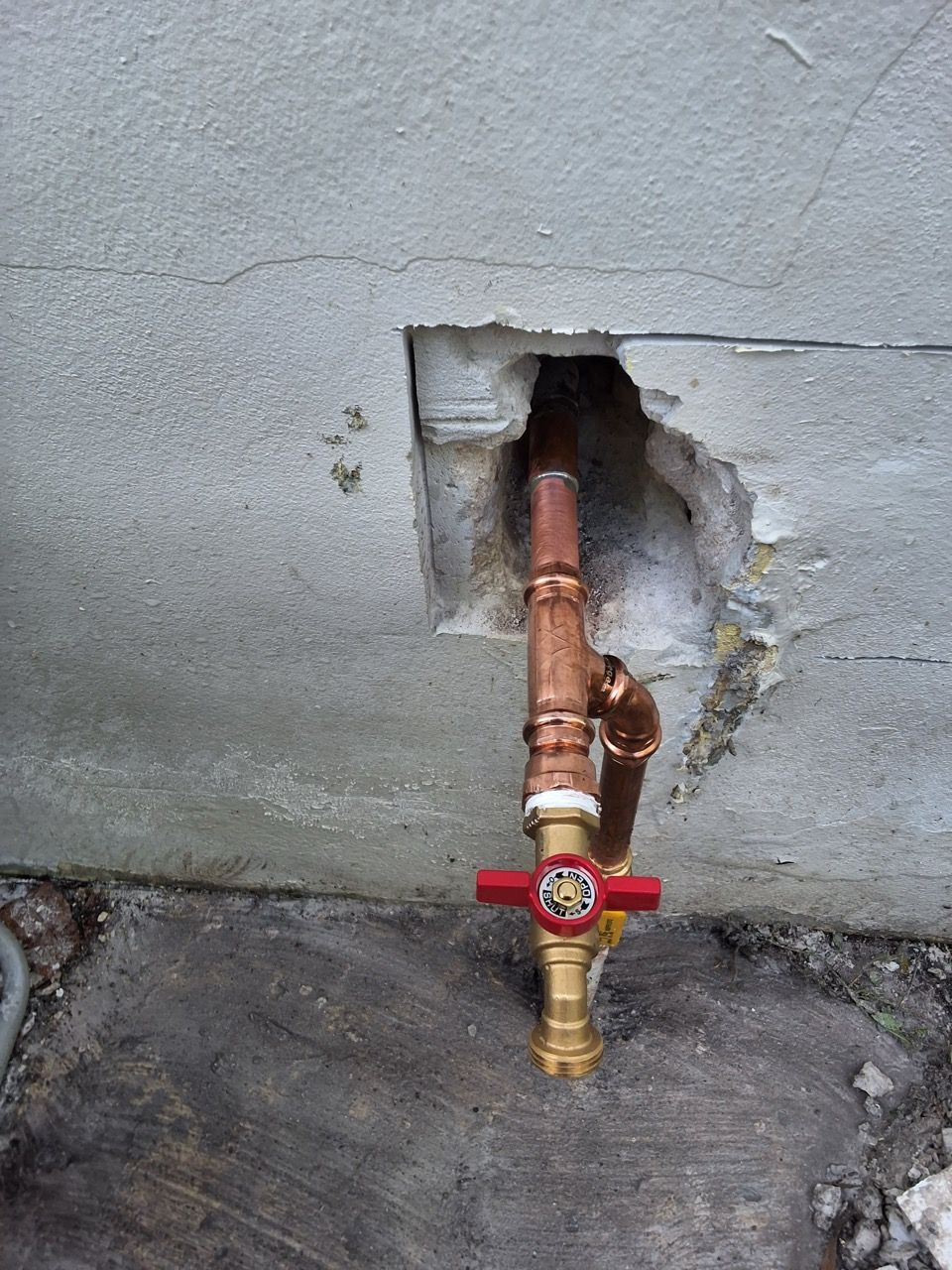 Copper pipe and shutoff valve protruding from a hole in a concrete wall, with a red handle.
