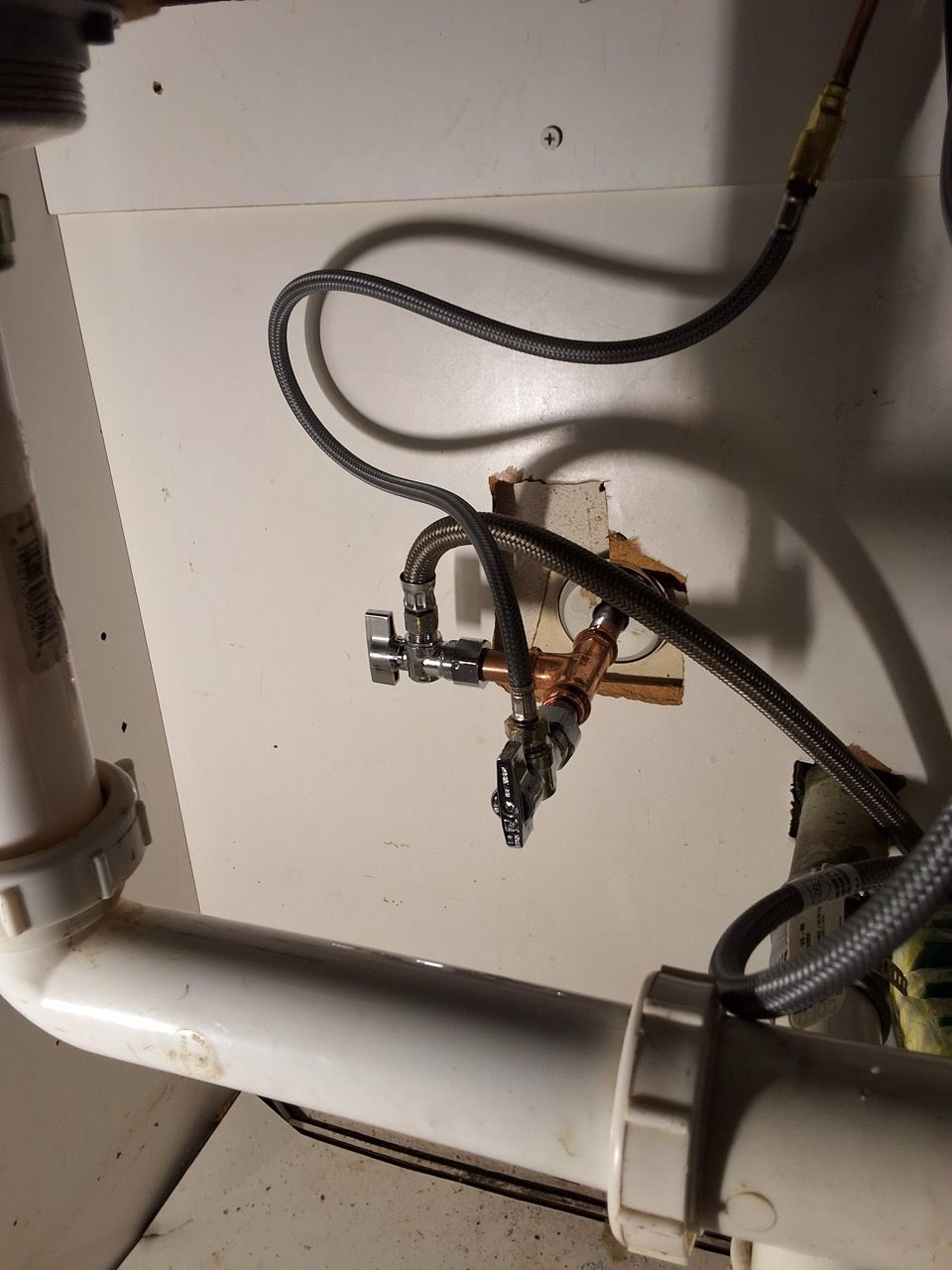 Plumbing pipes and valves under a sink, with braided hoses and white drain piping.