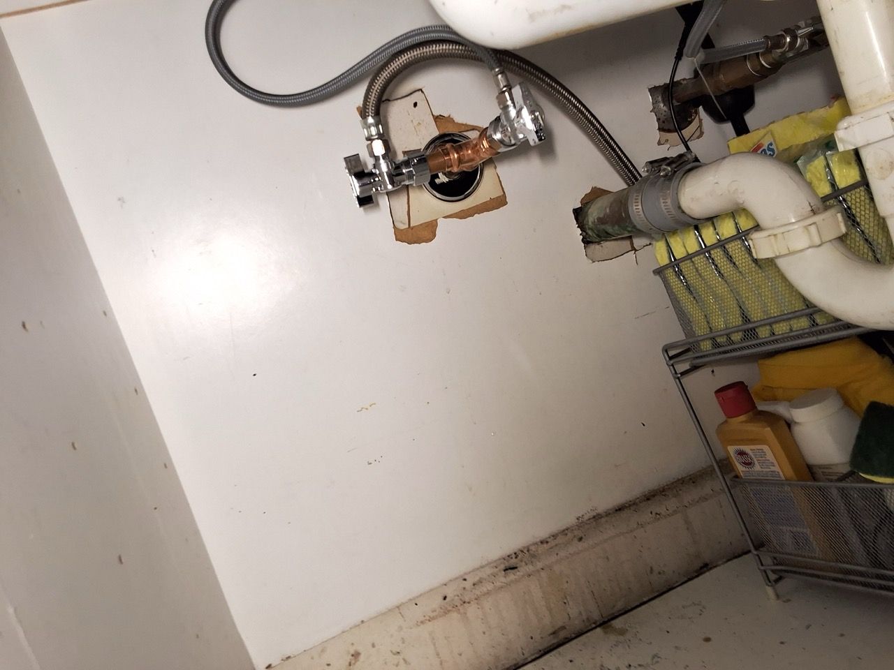 Partially exposed plumbing and pipes against a white wall in a utility or basement area