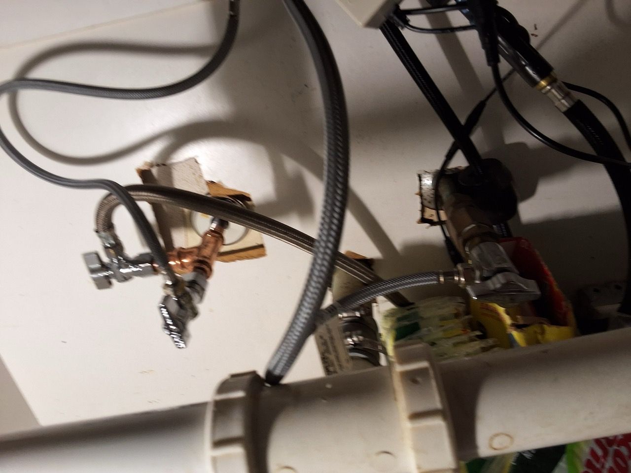 Under-sink plumbing with hoses, shutoff valves, and pipes against a wall