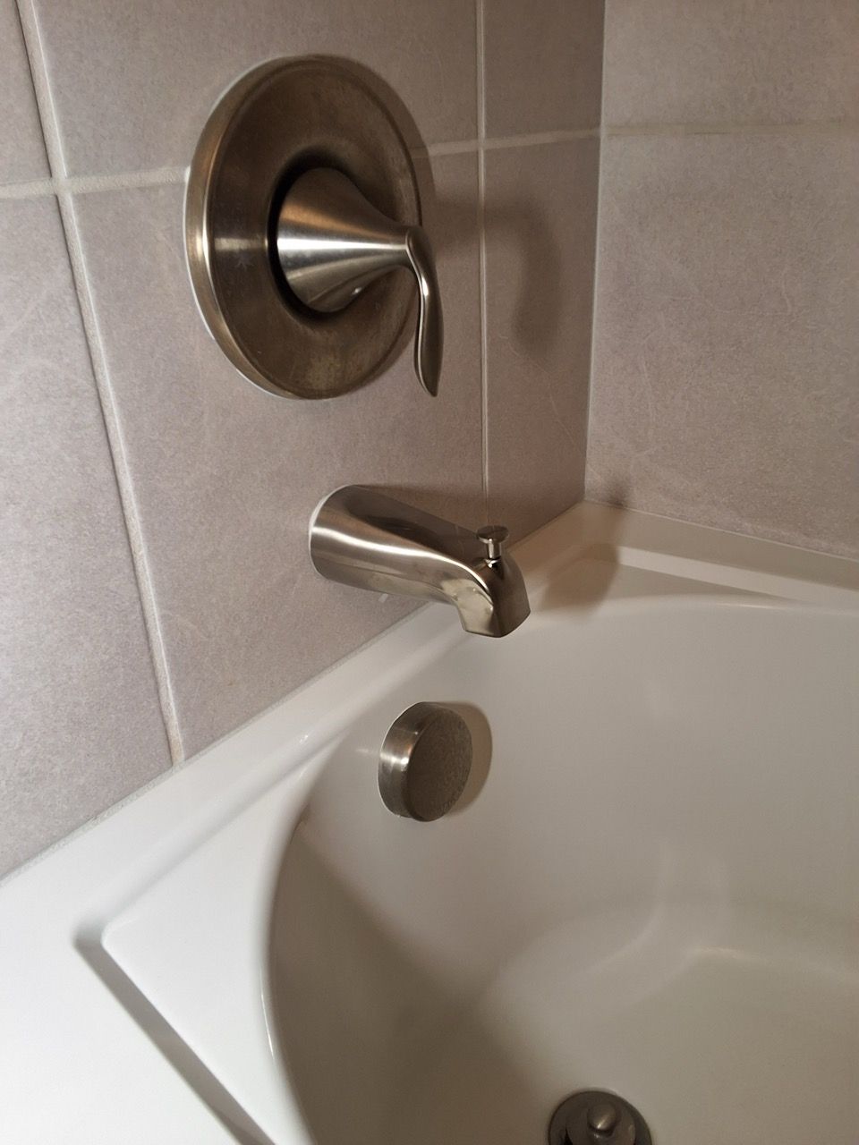 Chrome bathtub faucet and shower control above a white tub in a tiled bathroom