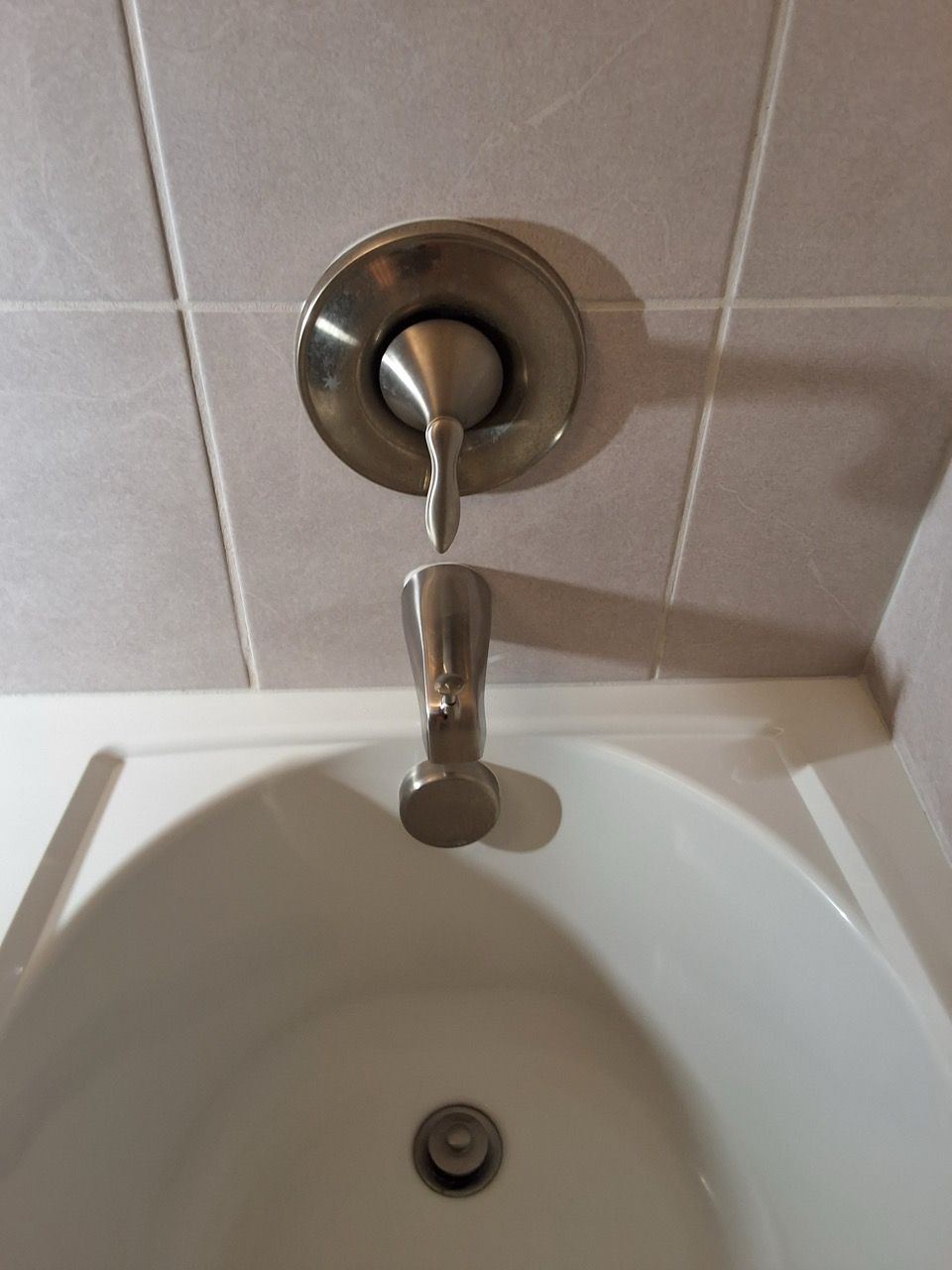 Chrome shower control above a white bathtub with a tiled wall background