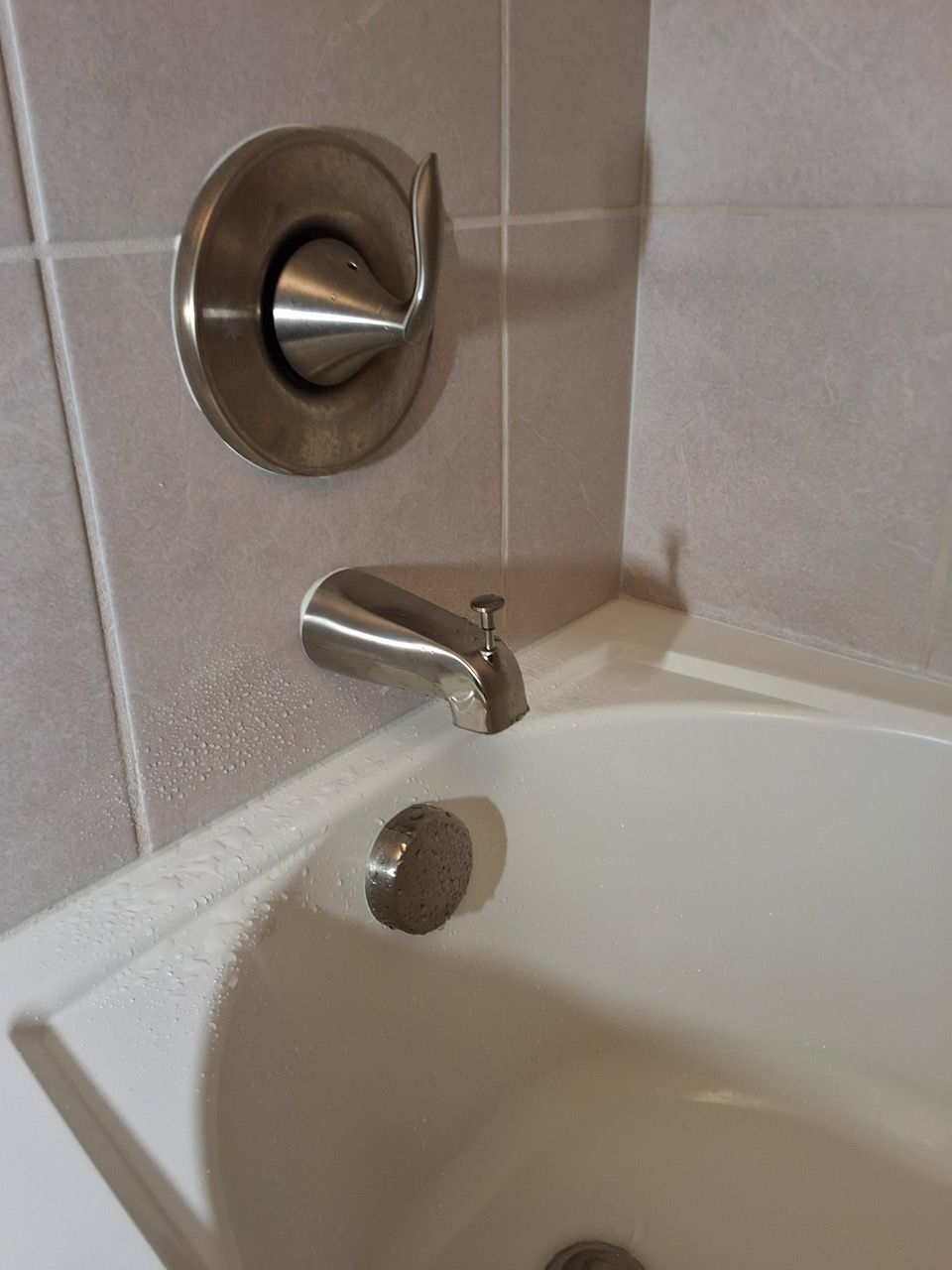 Bathtub corner with chrome shower controls, faucet, and overflow drain on beige tile wall