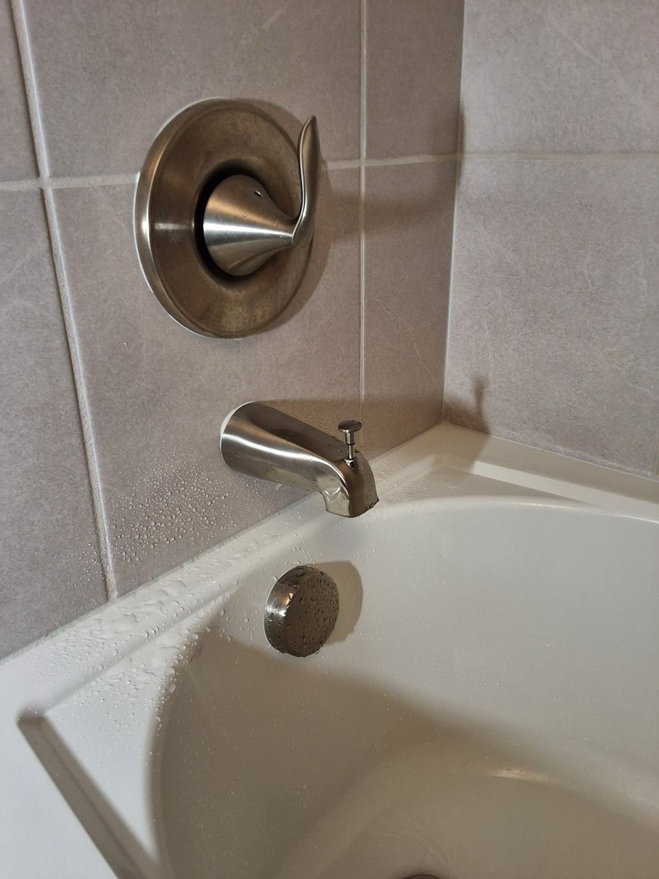 Bathtub faucet and shower valve on a tiled bathroom wall above a white tub