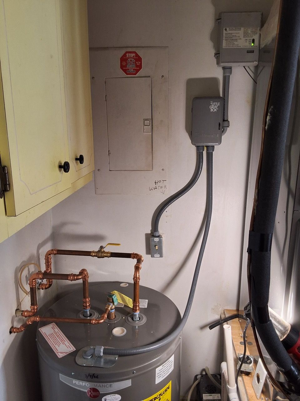 Water heater with copper pipes and electrical boxes in a utility closet.