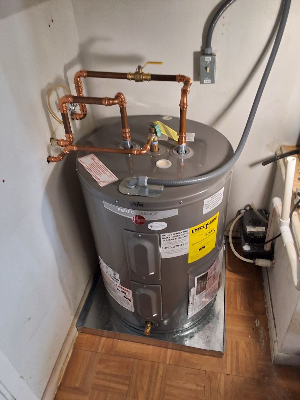 Water heater with copper pipes in a small utility closet beside wood flooring.