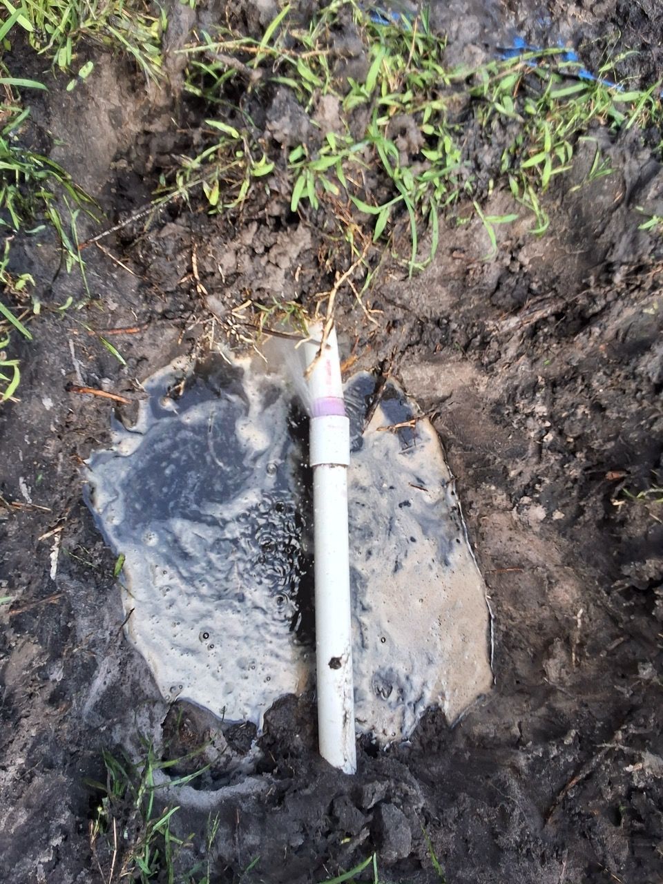White PVC pipe with a pink cap sticking out of a muddy hole in the ground