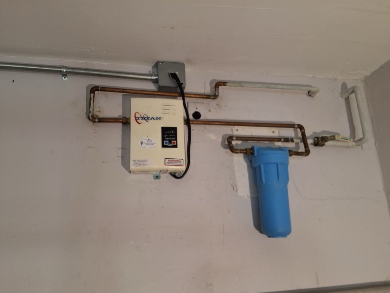 Wall-mounted water filter system with white and blue canisters connected to copper pipes on a white wall