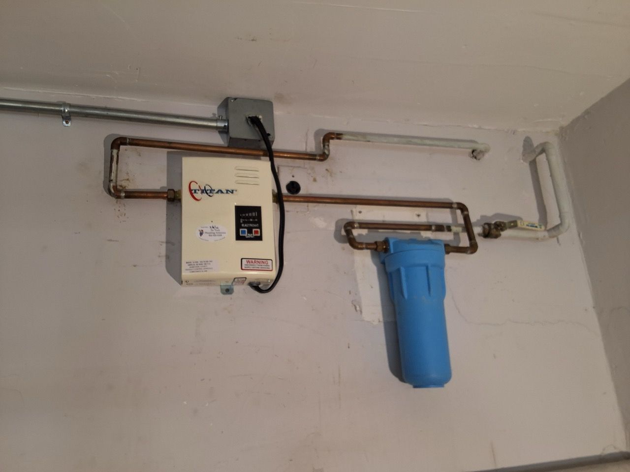 Wall-mounted water filter system with blue canister and beige control unit on a utility room wall