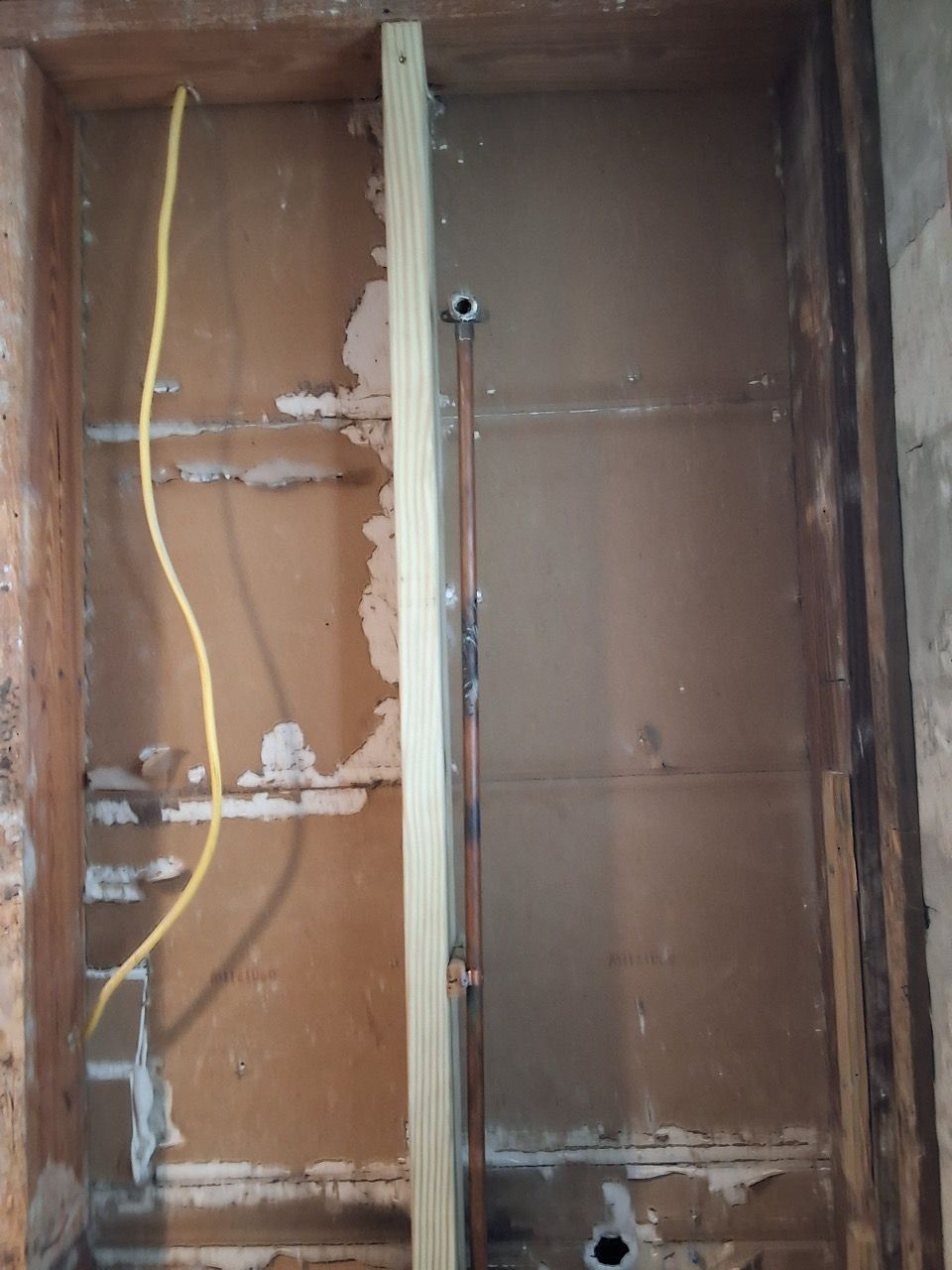 Exposed wall studs and wiring inside a damaged wall cavity with brown paneling.