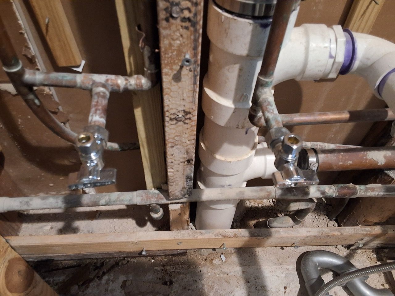 Exposed plumbing and PVC pipes inside a wall, with metal valves and copper lines visible.