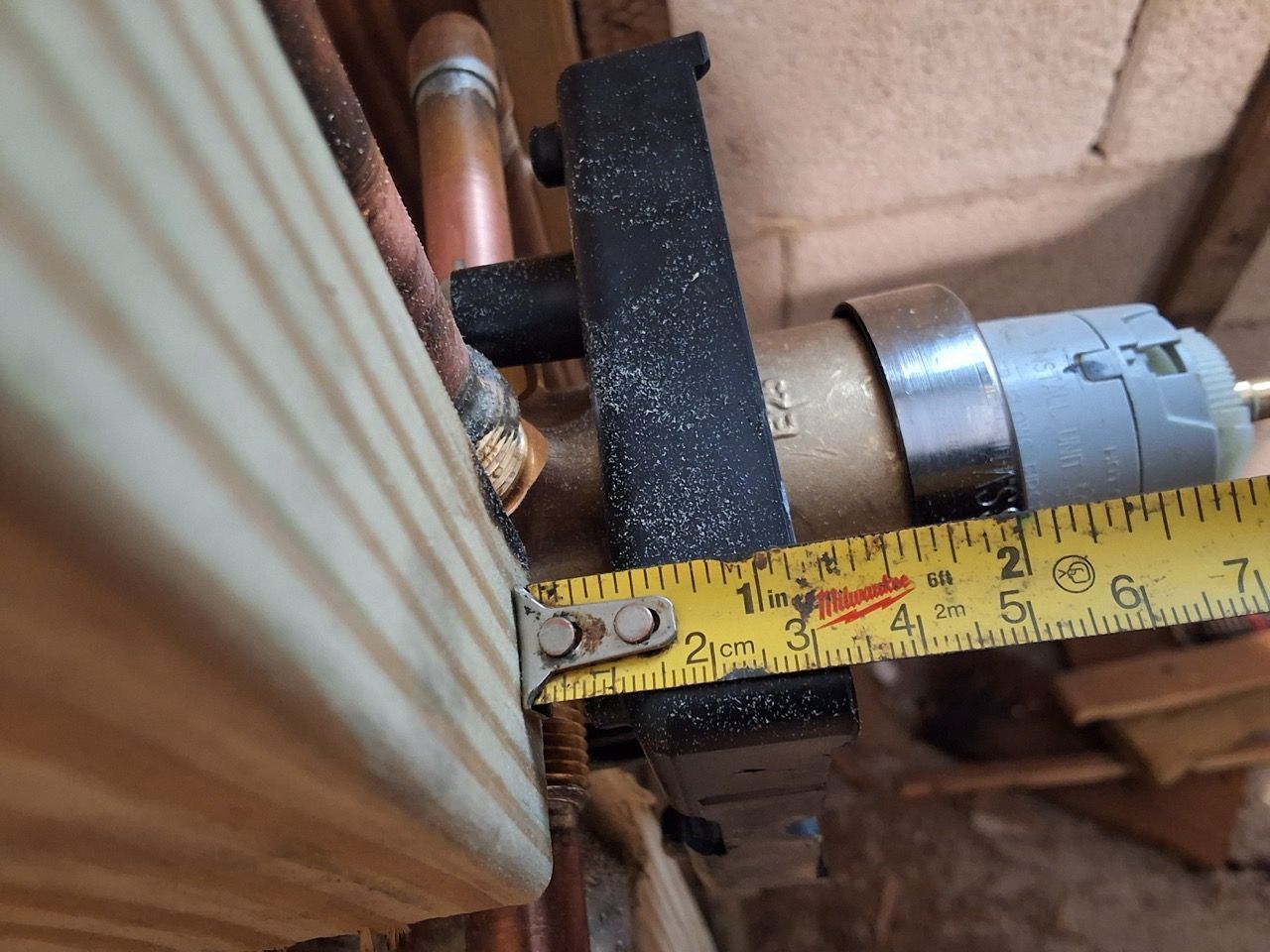 Tape measure between a ribbed panel and a metal motor assembly inside a machine compartment