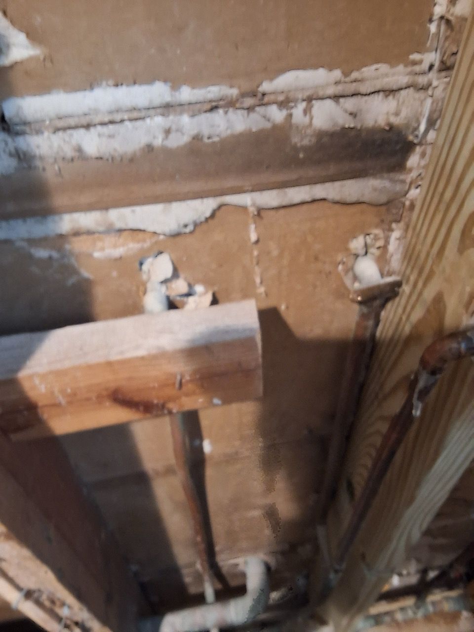 Exposed ceiling joists and pipes in a damaged wall cavity with insulation and wood framing visible