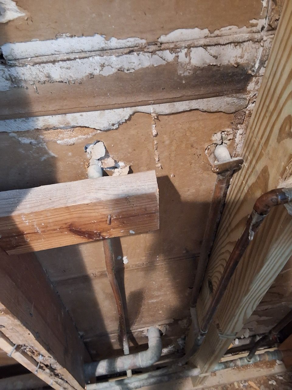 Exposed ceiling framing with wooden beams, pipes, and rough plaster in an unfinished interior.
