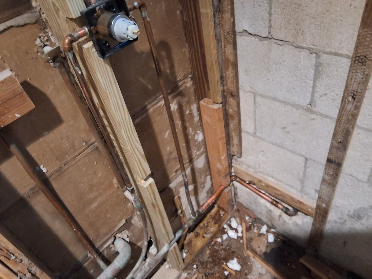 Exposed utility pipes and wiring in a basement corner beside cinderblock and wood framing.