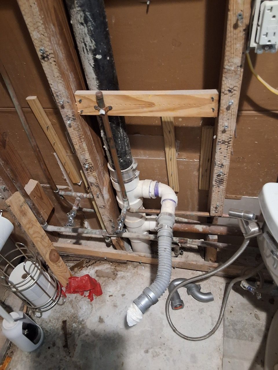 Open wall plumbing with white PVC pipes, black drain line, and exposed studs in a utility area