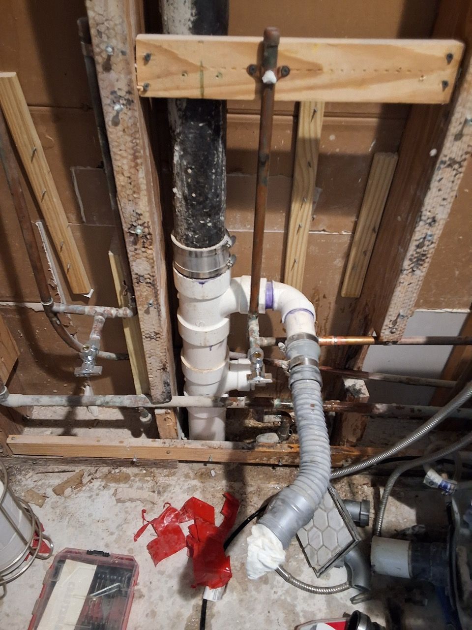 Exposed basement plumbing with white and gray pipes, a red paint mark on the floor, and unfinished wall framing