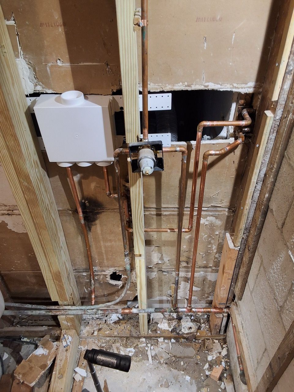 Damaged wall with exposed pipes and wiring during renovation, showing plumbing and electrical fixtures.