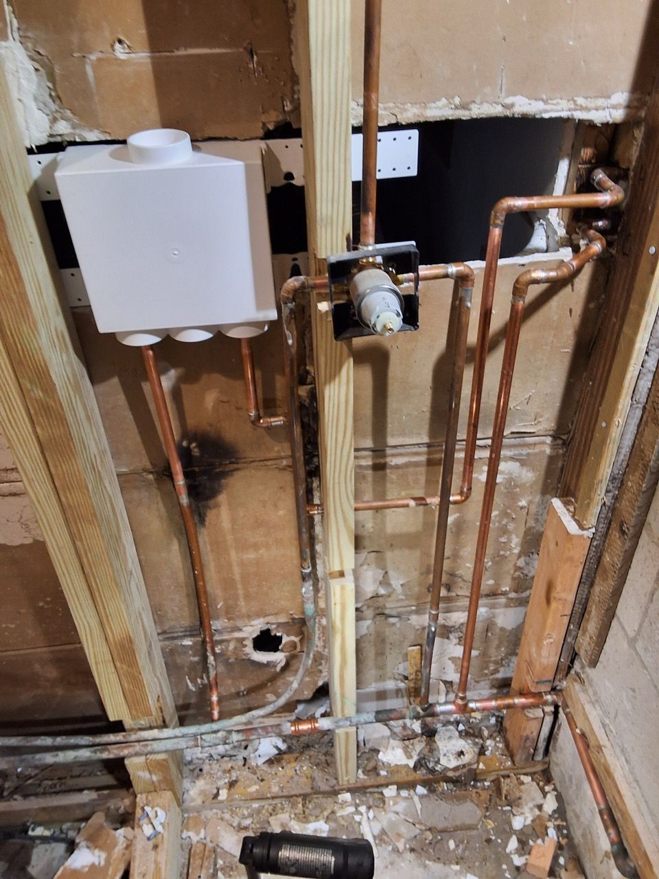 Exposed bathroom wall with plumbing pipes, water tank, and missing drywall during renovation