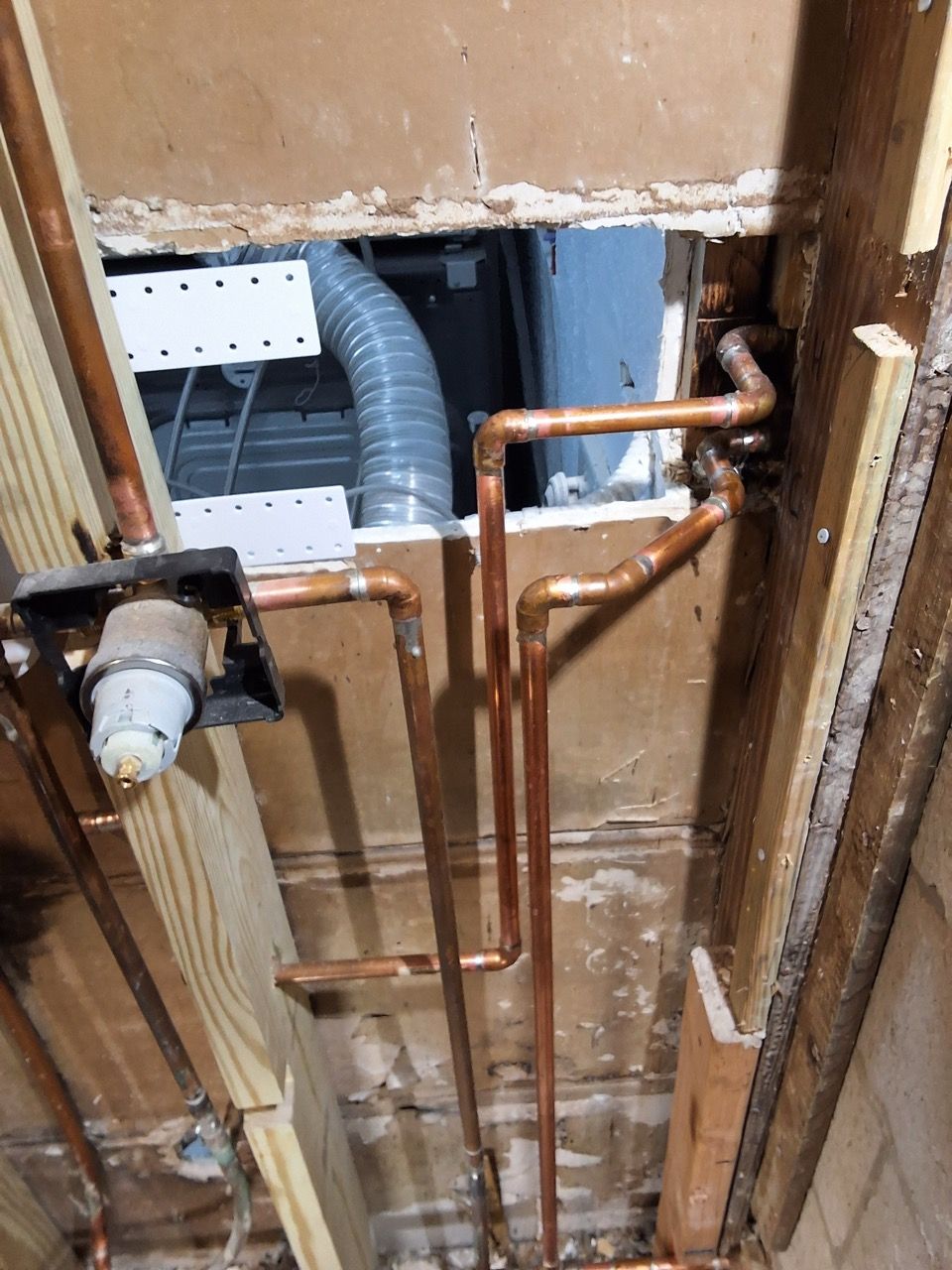 Exposed plumbing and copper pipes in a wall cavity under construction, with a gray vent hose and faucet hardware.