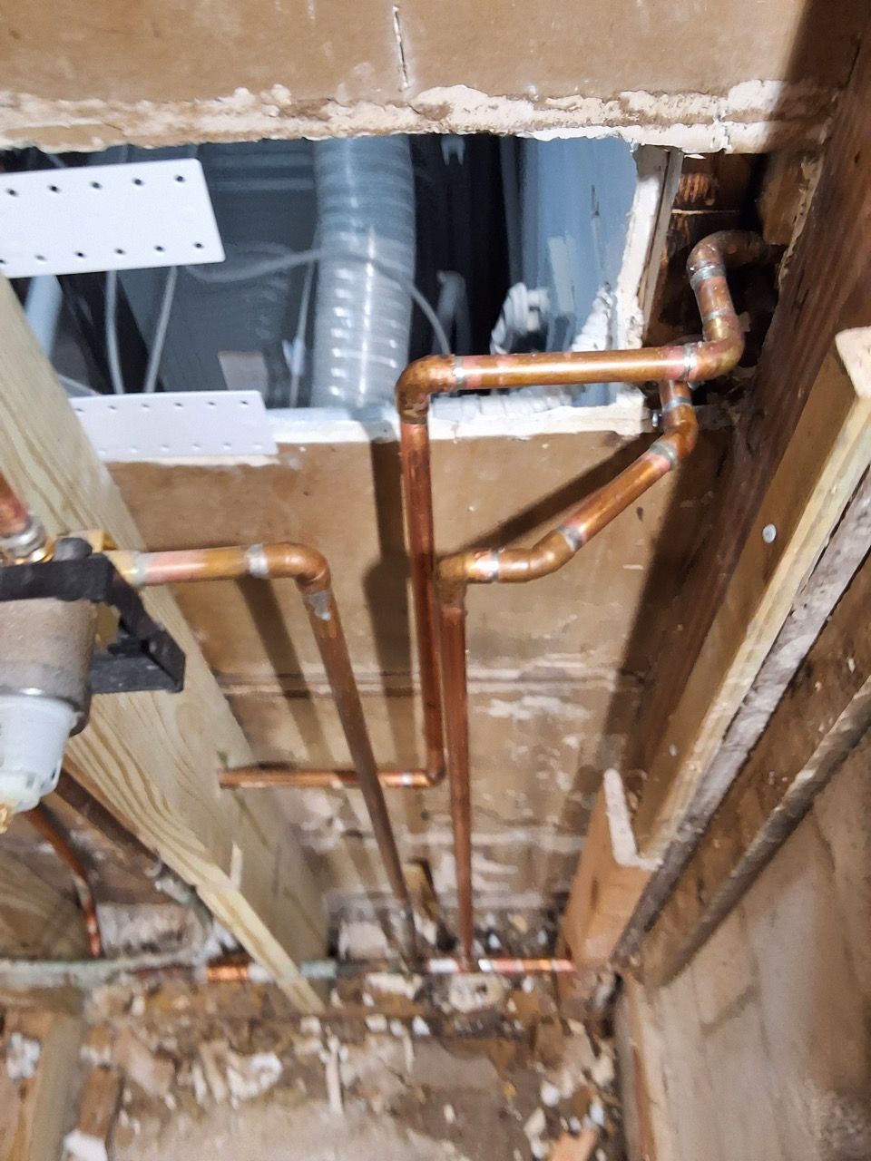 Exposed copper plumbing and ducts in an unfinished wall opening during renovation.