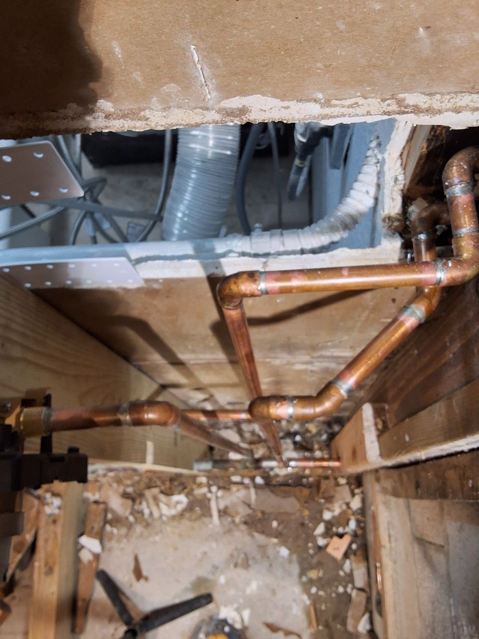 Exposed copper plumbing and gray ductwork in a damaged crawlspace with debris on the floor