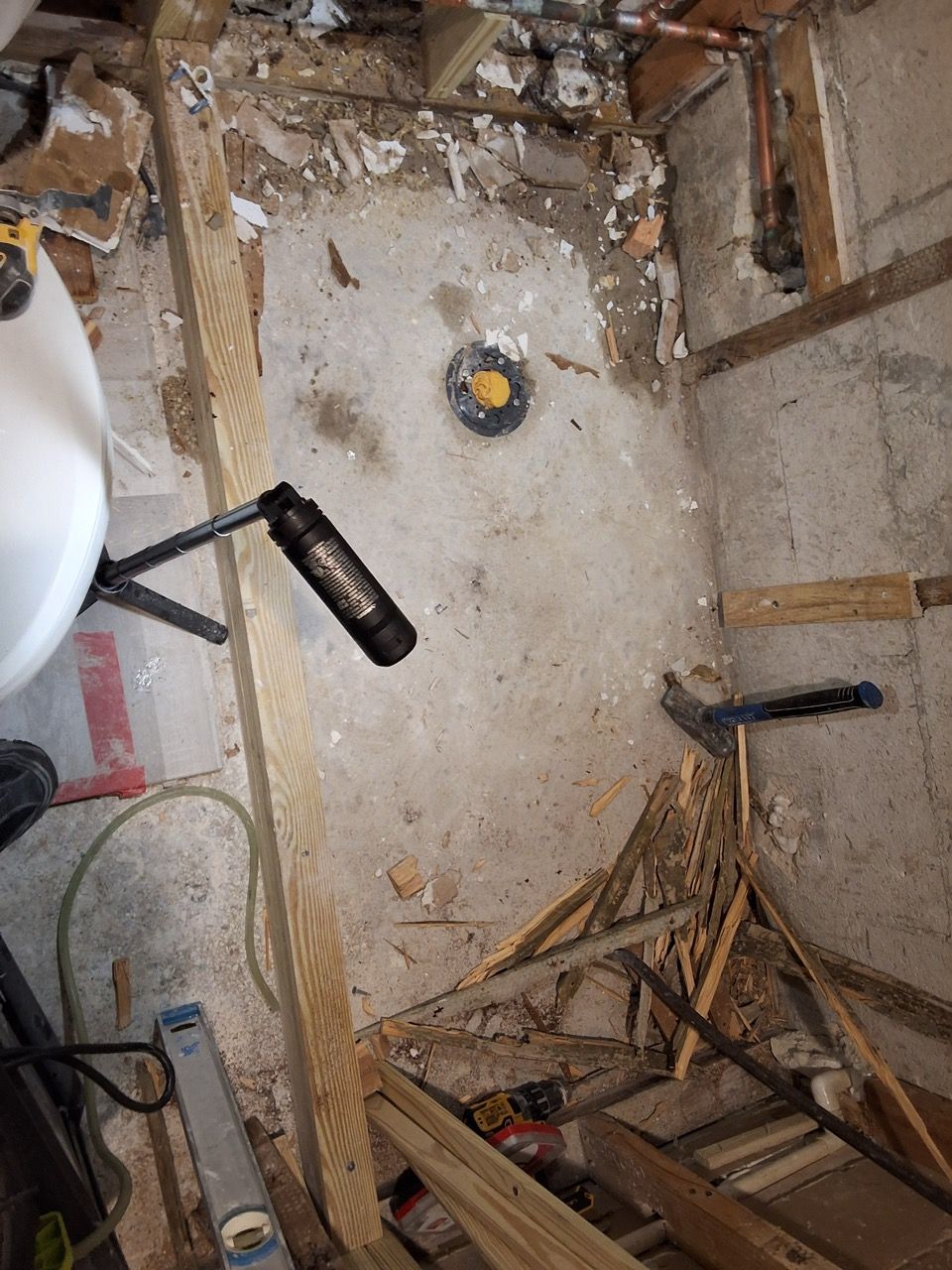 Damaged bathroom floor with exposed subfloor, debris, and a sink edge visible on the left