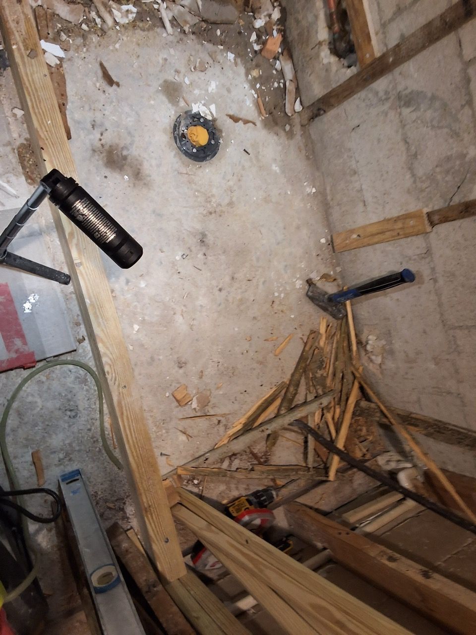 Cluttered unfinished room with exposed beams, debris, a flashlight, and a yellow electrical outlet on the wall