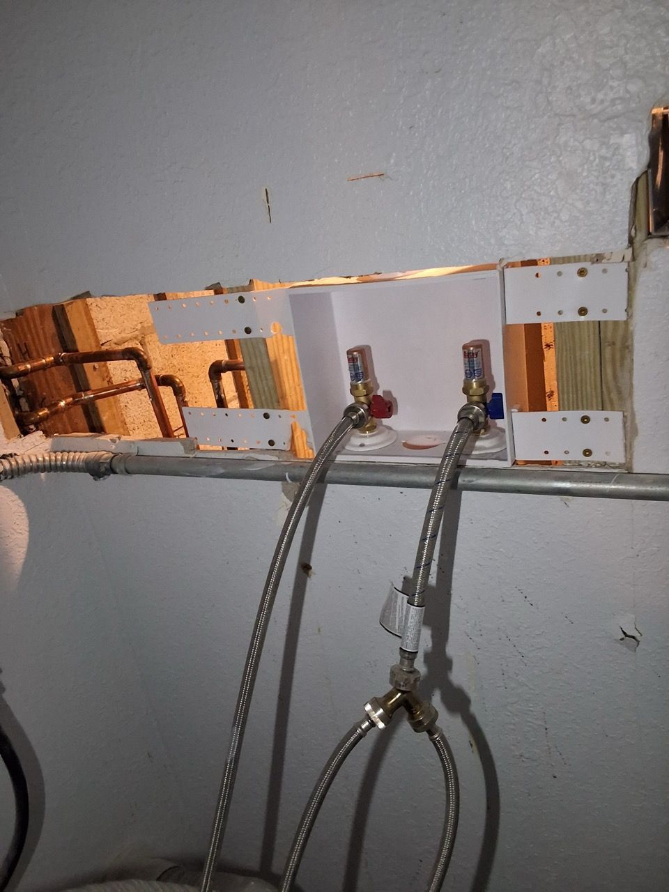 Exposed plumbing pipes and valves protruding through a wall opening with wiring hanging below