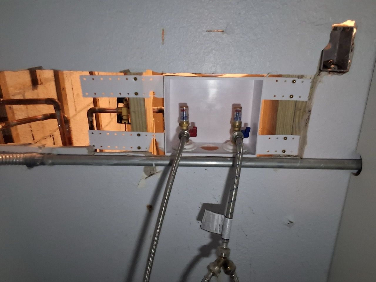 Open wall with exposed studs, pipes, and electrical wiring, showing unfinished interior construction.