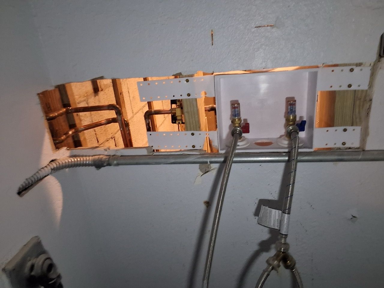 Exposed wall wiring and electrical boxes during renovation, with cables hanging from an unfinished drywall opening