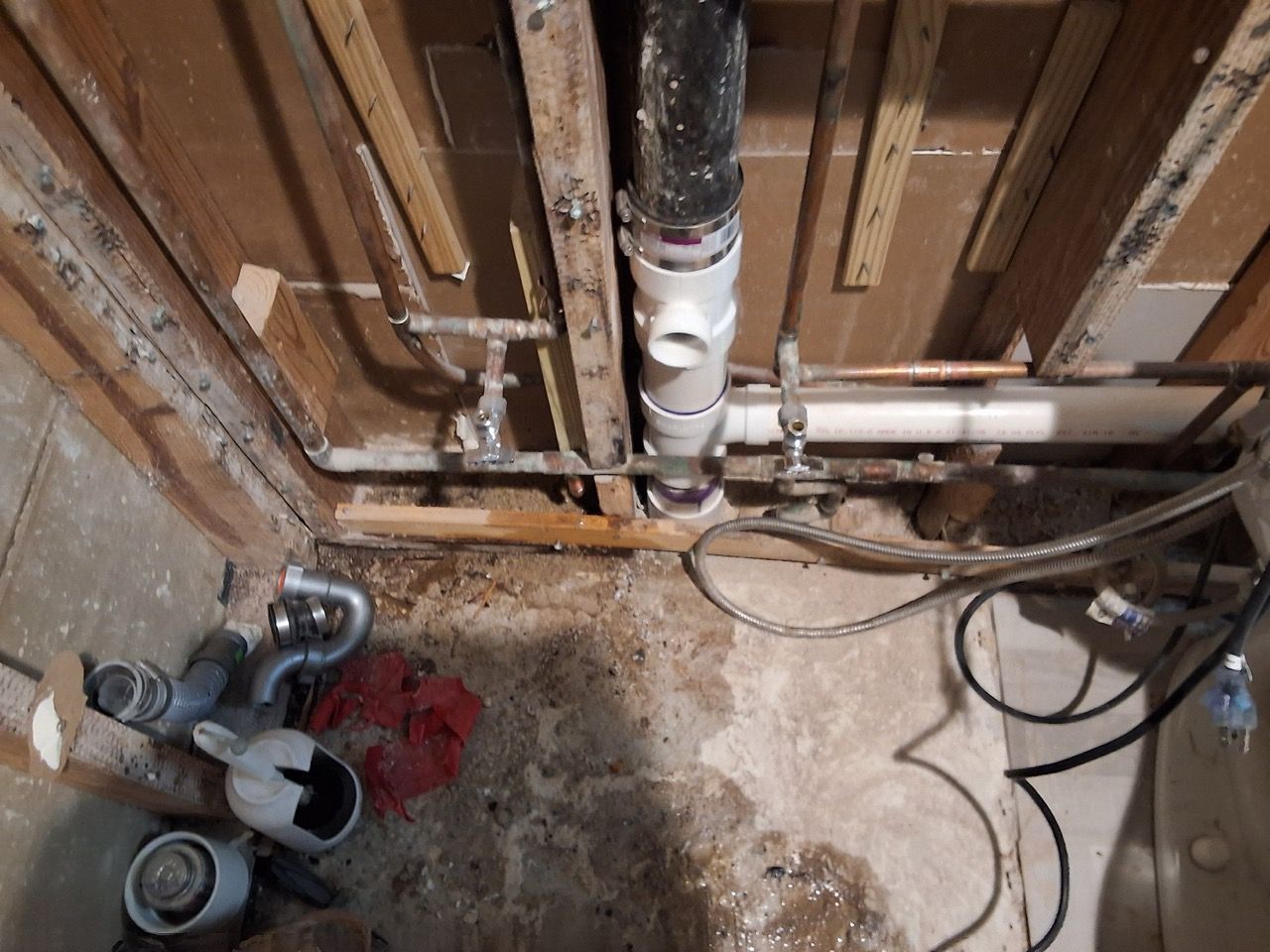 Unfinished basement with exposed pipes, wood framing, and tools on a concrete floor