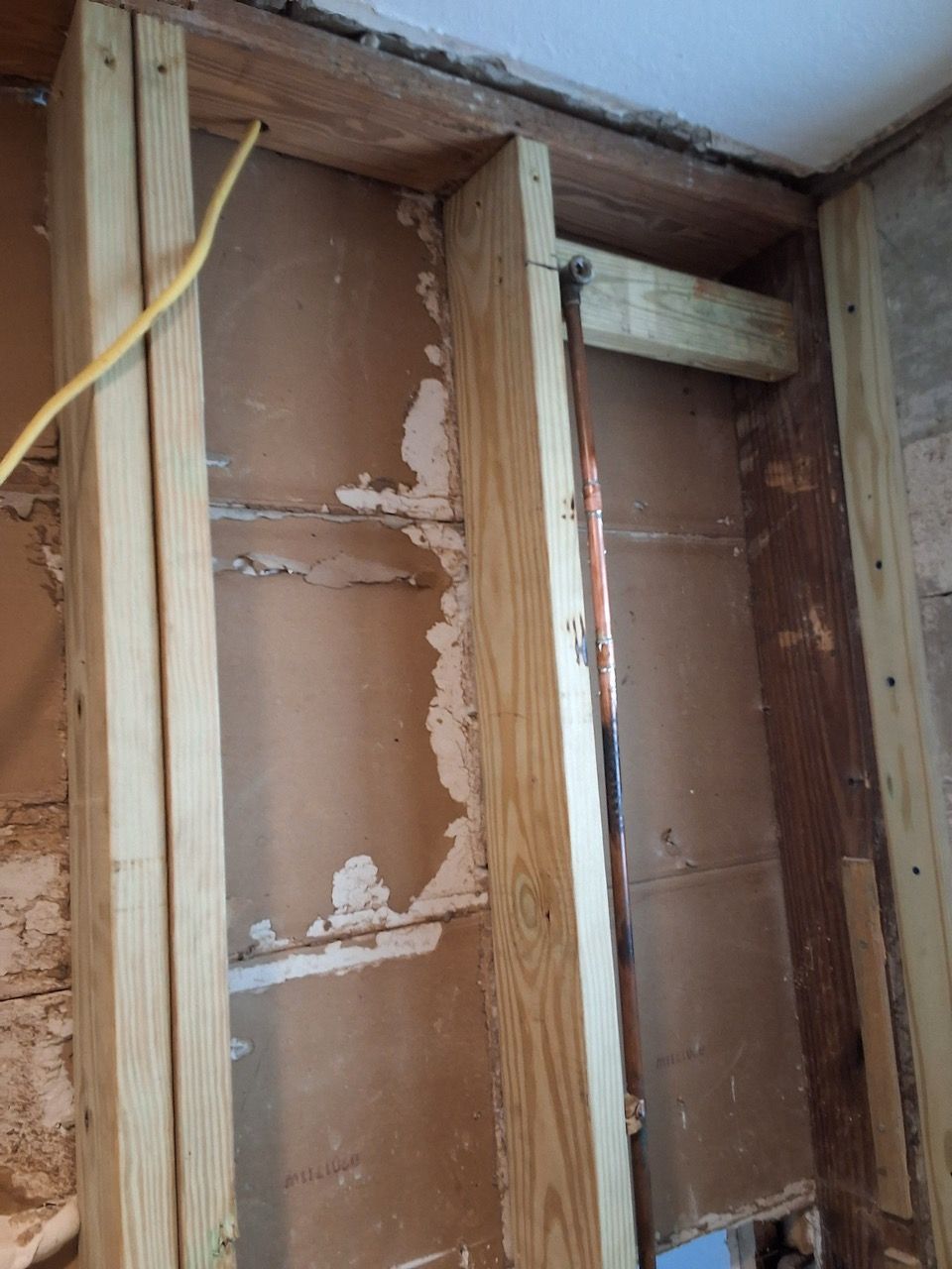 Exposed wall framing with brown sheathing and a yellow cable inside an unfinished room.
