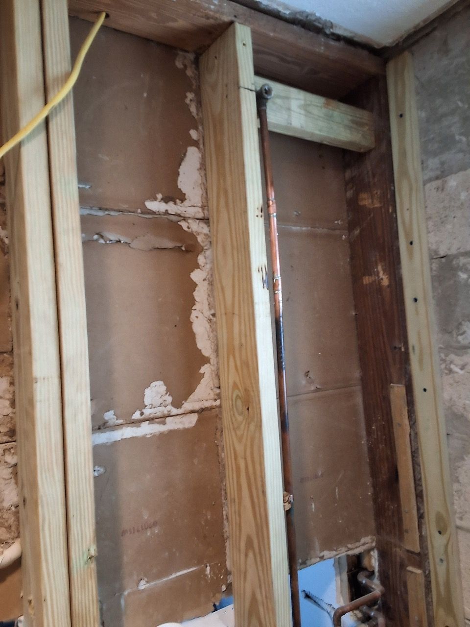 Partially stripped interior wall framing with exposed studs, brown insulation, and damaged drywall patches