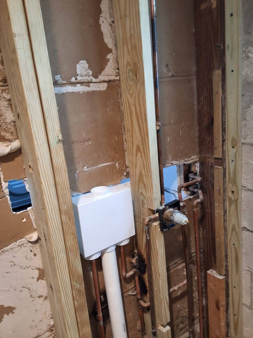 Open wall with exposed plumbing, wood studs, and white utility boxes during renovation