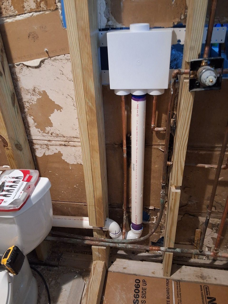 White wall-mounted tank and vertical PVC pipes in an unfinished wall cavity.
