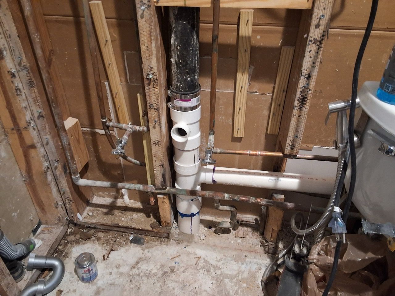 Exposed plumbing pipes and fittings inside a basement wall under construction, with debris on the floor.