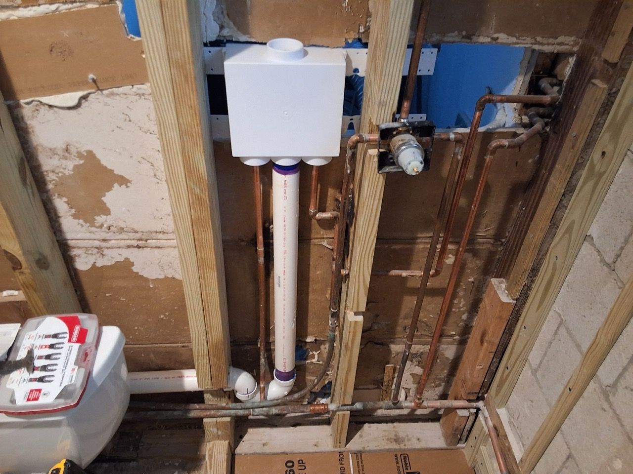 Partially renovated bathroom wall with exposed plumbing and a white wall-mounted tank.