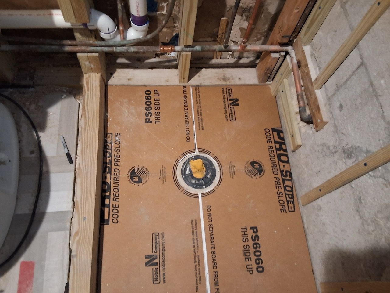 Cardboard floor protector in a basement bathroom under construction, beside exposed plumbing and framing.