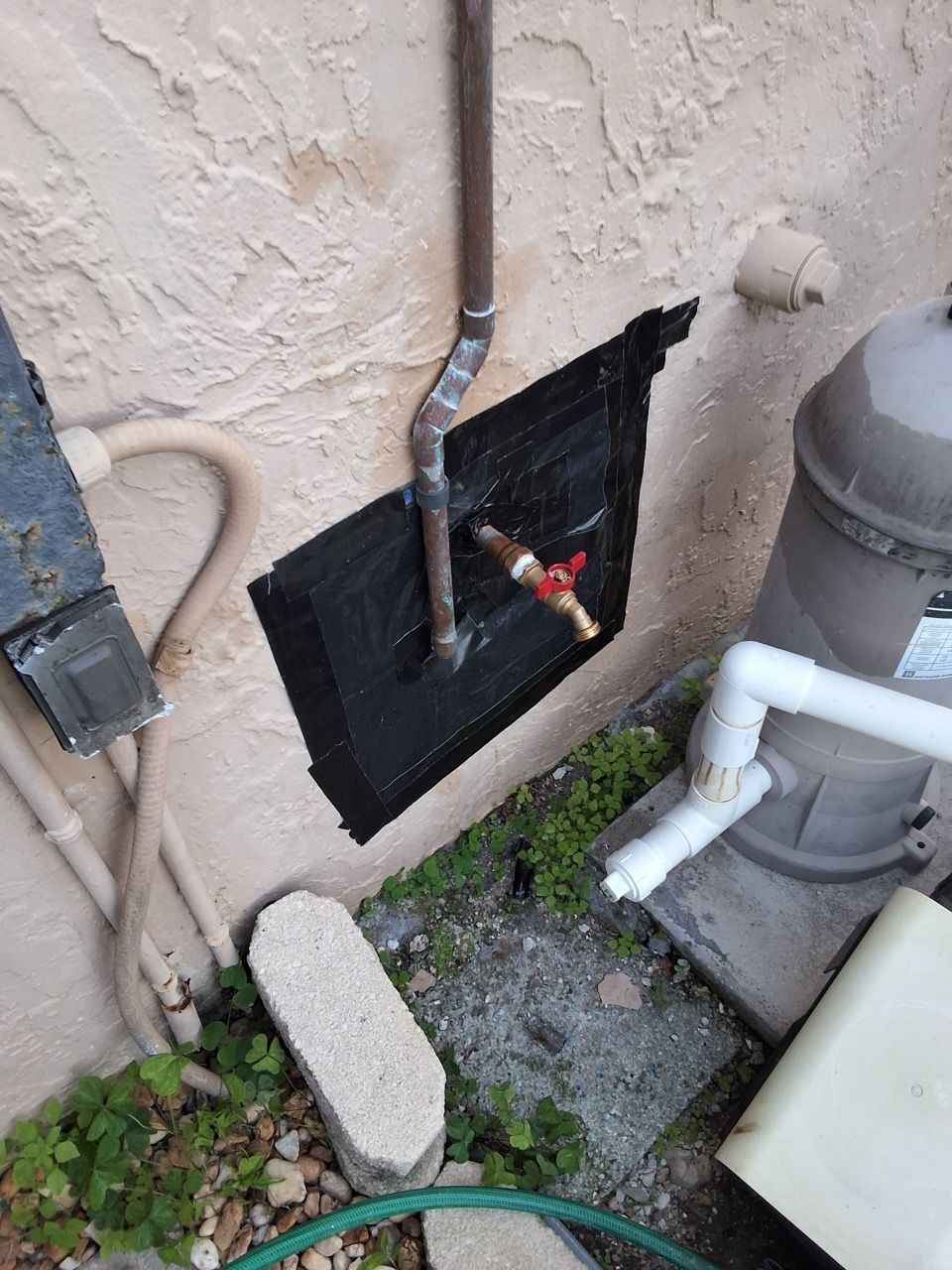 Wall-mounted plumbing with exposed pipes and valve near a stucco exterior wall.