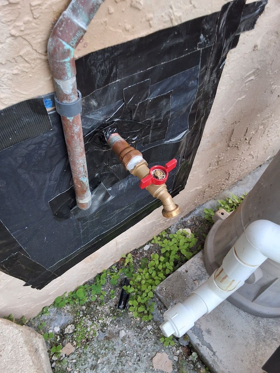 Outdoor utility pipes and a water valve on a wall with black waterproofing and gravel below